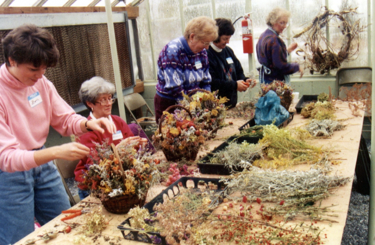 five people building wreaths behind a table covered in greens and plant parts