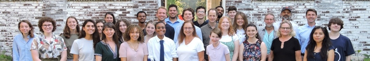 A group image of students, faculty, and staff in front of the archway of a brick building