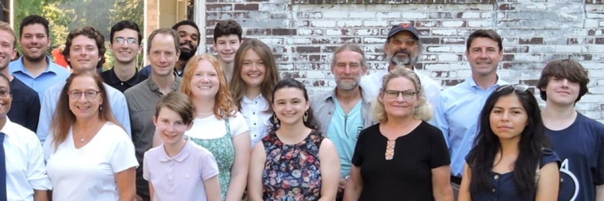 A group image of students, faculty, and staff in front of the archway of a brick building