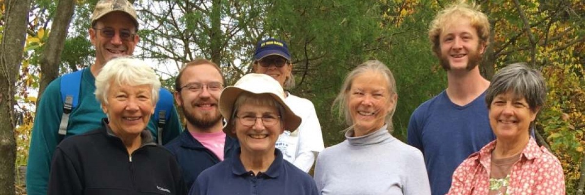 8 people dressed in casual clothes pose in front of trees with yellowing leaves